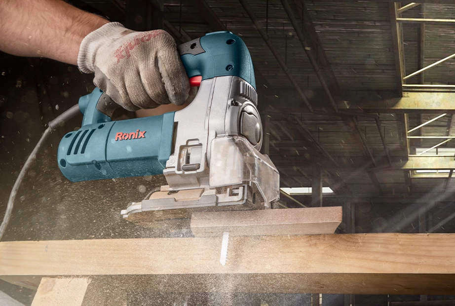 A man wearing protective gloves uses a Ronix jigsaw on wood